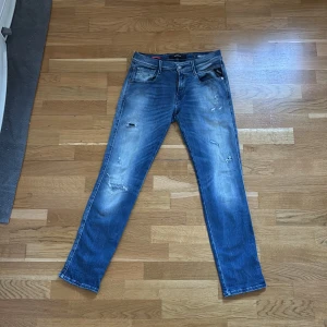 Replay Hyperflex Anbass jeans blå - Säljer ett par Replay Hyperflex Anbass jeans i blå tvätt med slitningar och snyggt slitna detaljer. Jeansen har klassisk femficksdesign, smal passform och stretchigt material för extra komfort. Perfekta för dig som gillar en modern och avslappnad look. En viktig sak att nämna är att etiketten på insidan dock saknas. Storleken är 30/31 men passar även den som har 30 i längd. Pris kan diskuteras och vid frågor och funderingar kan ni skriva. 
