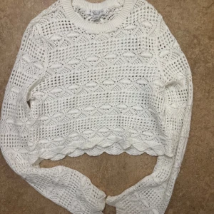 Vit stickad croppad tröja  - Säljer en vit stickad croppad tröja med snyggt hålmönster. Tröjan har lång ärm och vida ärmar i slutet. Den är köpt från newyorker och är i storlek M, men funkar även för en s, använd endast en gång. 