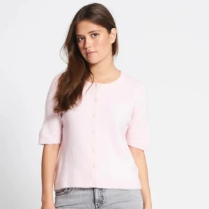 Ljusrosa kofta med pärlknappar - Superfin ljusrosa kofta med korta ärmar och rund hals. Koftan har söta pärlknappar hela vägen framtill och är gjord i ett mjukt, stickat material. Perfekt att slänga över en topp för en söt och chill look.