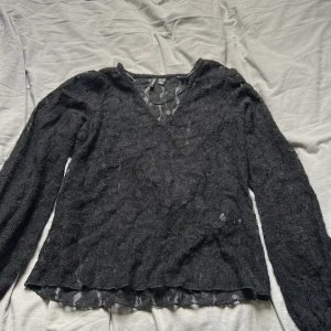 Svart spetsblus från Vero Moda - Säljer en svart långärmad blus från Vero Moda i transparent spets med v-ringning. Toppens material är lätt och har ett snyggt mönster i spetsen, perfekt för att skapa en cool lager-på-lager-look. Använd en gång