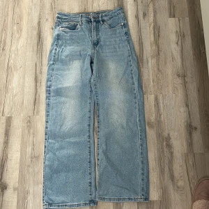 Ljusblå wide jeans med raka ben - Säljer ett par ljusblå jeans med raka, vida ben och klassiska femficksdetaljer. Jeansen har hög midja och är tillverkade i bomullsdenim med snygg tvätt och kontrastsömmar. Perfekta för en avslappnad och trendig look.