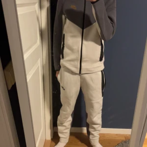 Vita mjukisbyxor från Nike - Säljer ett par vita mjukisbyxor från Nike med svarta detaljer längs sidorna. Byxorna har en avslappnad passform och är perfekta för chill eller träning. Klassisk Nike-logga på benet och elastisk midja för extra komfort.