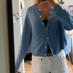 Blå stickad kofta med knappar - Mysig blå stickad kofta med långa ärmar och flera vita knappar framtill. 