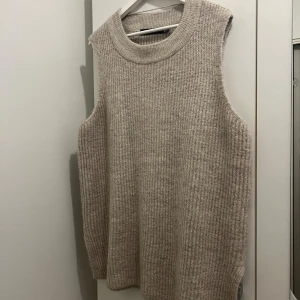 Beige stickad väst från Vero Moda - Beige stickad väst från Vero Moda i storlek XL. Västen har en grov ribbad struktur, rund halsringning och slits i sidorna för en snygg och avslappnad look. Perfekt att slänga över en skjorta eller t-shirt för extra lager.