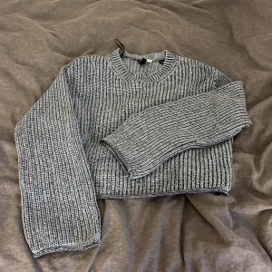 Grå stickad tröja från H&M Divided XS - Säljer en ribbstickad grå tröja från H&M i storlek XS. Tröjan har en croppad passform, rund halsringning och långa ärmar. Perfekt för lager-på-lager och chill dagar. Snyggt melerat garn i svart och vitt ger en cool look.
