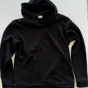Svart hoodie från Ciszere - Svart hoodie från Ciszere med broderad logga på bröstet. Tröjan har stor huva, lång ärm och en klassisk känguruficka framtill. Tillverkad i mjukt material som passar perfekt för kyligare dagar.