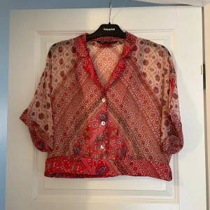 Zara Mönstrad röd skjorta  - Säljer en luftig och transparent skjorta från Zara i rött och beige med orientaliskt inspirerat mönster. Skjortan har korta ärmar, knappar framtill och en avslappnad passform. Perfekt för dig som gillar färg och unika prints!