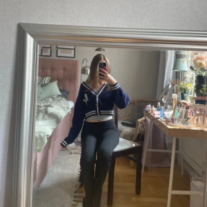 Mörkblå croppad kofta från H&M - Säljer en mörkblå croppad kofta från H&M Divided med vita ränder och broderad NY-logga på bröstet. Koftan har v-ringning, knappar framtill och långa ärmar. Perfekt för lager-på-lager och snygg till både jeans och kjol.