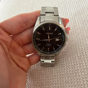 Silverfärgad Champion Spider klocka - Stilren klocka från Champion med svart urtavla och datumvisning. Modellen heter Spider och har en robust länk i silverfärgat metall. Perfekt accessoar för dig som gillar klassisk design och tydliga detaljer.