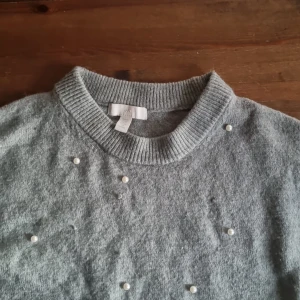 Grön stickad tröja med pärlor H&M XS - Mysig grön stickad tröja från H&M i storlek XS. Tröjan har rund halsringning, ribbade muddar och är dekorerad med små pärlor framtill för en extra touch. Perfekt för dig som gillar stilrena detaljer och vill ha något som sticker ut lite.