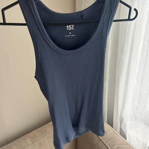 Blå ribbad linnetopp från 157 - Säljer en blå ribbad linnetopp från 157 i storlek XS. Toppen är ärmlös med rund halsringning och har en tight passform. Perfekt att styla med jeans eller kjol för en enkel och snygg look.