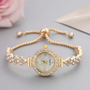 Guldig klocka med strass och pärlemor - Snygg guldig klocka med rund urtavla i pärlemor och gnistrande strass runt både boett och armband. Justerbart armband med kulor i ändarna och elegant design som drar blickarna till sig.