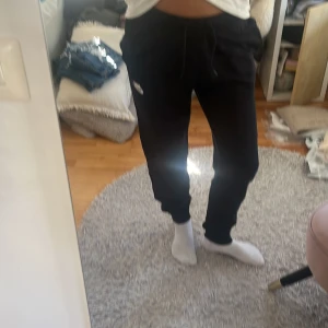 Svarta mjukisbyxor från Nike - Svarta mjukisbyxor från Nike med dragsko i midjan och resår vid bensluten. Byxorna har en avslappnad passform och en liten vit Nike-logga på ena benet. Perfekta för chill eller träning.