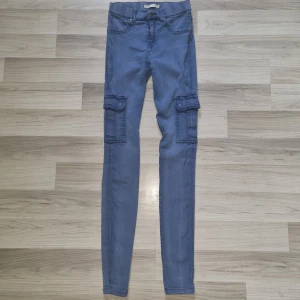 Blå vintage cargobyxa från lager157, stl M - Säljer ett par blå vintage cargobyxa från lager 157 i storlek M. Byxorna har smal passform, stora fickor på sidorna av benen och klassisk knappstängning. Materialet är mjukt och stretchigt, perfekt för en avslappnad streetstil. Har en rispa på vänster knä (se bild)