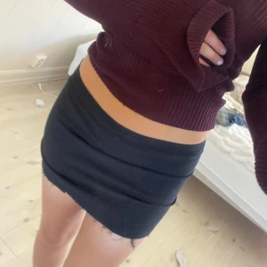 Svart tight minikjol med rå kant - Svart kortkjol med tight passform och rå, fransig nederkant. Kjolen har en enkel design utan mönster och stängs med dragkedja i sidan. Perfekt för dig som gillar en clean och edgy stil.