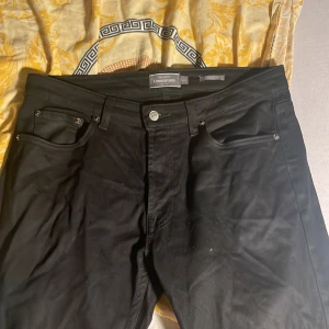 Svarta regular fit jeans från Dressmann - Svarta jeans från Dressmann i regular fit med klassisk femficksdesign. Byxorna har raka ben och normal passform, tillverkade i ett slitstarkt bomullsmaterial. Perfekta för dig som gillar en enkel och stilren look.