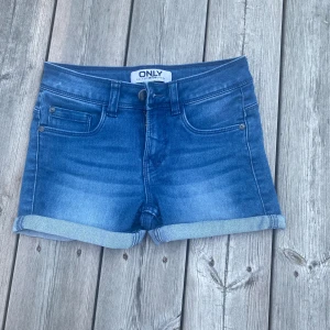 Blå jeansshorts från ONLY XS - Snygga blå jeansshorts från ONLY i storlek XS. Klassisk femficksmodell med uppvikta benslut och knapp- samt dragkedja framtill. Shortsen har en normal passform och är tillverkade i mjukt jeanstyg som är perfekt för varma dagar.