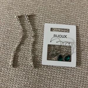 Set med örhängen från Bijoux - Säljer ett snyggt set med örhängen från Bijoux. Ett par långa, glittriga örhängen i silverfärg och ett set med tre ringörhängen, varav ett par har gröna droppformade stenar och ett par har dekorativa detaljer. Perfekt för att lyfta din stil.
