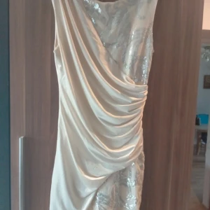  festklänning  med paljetter - Säljer en kort champagnefärgad klänning med snygg omlott-drapering och glittriga paljettdetaljer. Köpt på Vinted, helt nytt skick. Står inget märke!👩‍❤️‍👩👩‍❤️‍👩🥂🥂