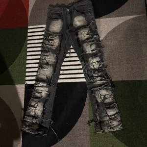 Svarta slitna jeans med trasiga detaljer - Riktigt coola svarta jeans med massor av slitningar och trasiga detaljer längs hela benen. Jeansen har en skinny passform och är tillverkade i denim med en tvättad look. Perfekta för dig som vill sticka ut och gillar en edgy streetstyle.