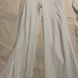 Vita bootcut byxor med hög midja - Snygga vita byxor med bootcut-ben och bred, vikbar hög midja. Byxorna har en mjuk och stretchig känsla, perfekta för en trendig och bekväm look. Passar dig som gillar stilrena och enkla plagg med en twist.