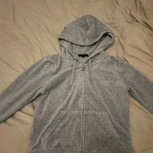 Grå hoodie från Juicy Couture - Säljer en grå hoodie från Juicy Couture i storlek S. Tröjan har dragkedja, huva med snörning och två fickor framtill. Liten broderad logga på bröstet. Perfekt för chill dagar eller när du vill vara extra comfy.