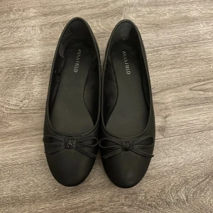 Svarta ballerinaskor från Anna Field - Klassiska svarta ballerinaskor från Anna Field med rund tå och dekorativ rosett framtill. Skorna är i ett slätt material som ger en stilren look och passar perfekt till både jeans och klänning. Aldrig använda!! ❤️