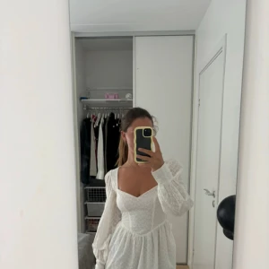 Vit omlottklänning med öppen rygg - Superfin vit kortklänning med broderade detaljer, v-ringning och långa puffärmar. Klänningen har öppen rygg med knytband och markerad midja. Perfekt för studenten!