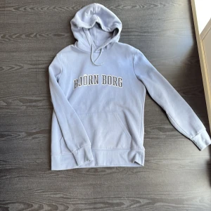 Ljusblå hoodie från Björn Borg - Snygg ljusblå hoodie från Björn Borg med stor logga framtill. Tröjan har huva med snörning, magficka och långa ärmar. Tröjan är i storlek L 