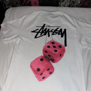 Vit Stüssy t-shirt med rosa tärningar - Säljer en stussy t shirt i fint skick. Tyvär så var den lite stor på mig. 