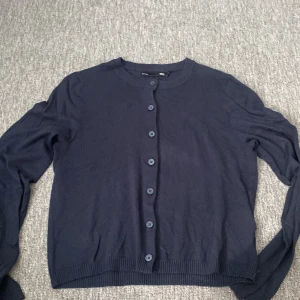 Mörkblå kofta från 157, storlek S - En klassisk mörkblå kofta från 157 med rund halsringning och knappar framtill. Koftan har långa ärmar och ribbade muddar vid ärmslut och nederkant. Knappt använd