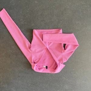 Rosa ribbad croppad polotopp - Trendig rosa polotopp med croppad passform och långa ärmar. Toppen är ribbad för en snygg struktur och har en tight siluett som framhäver figuren. Perfekt för dig som gillar färg och vill sticka ut lite extra.