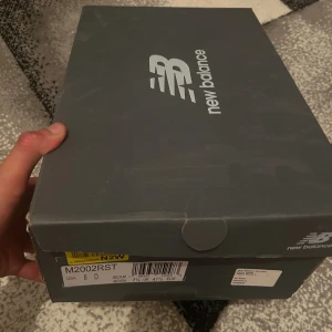 New Balance 2002R grå sneakers - Säljer ett par New Balance 2002R sneakers i snygg grå färg. Skorna har meshpaneler och detaljer i mocka, med klassisk N-logga på sidan. Sulan är vit med grå inslag och skorna har snörning. Perfekta för dig som gillar stilrena och bekväma sneakers.