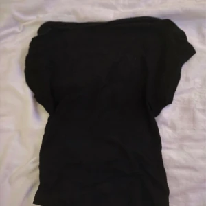 Svart topp öppen i ryggen - Säljer en svart topp med korta ärmar och en enkel, stilren design. Toppen har en bred halsringning som sitter snyggt över axlarna och är figurnära i modellen. Perfekt att matcha med jeans eller kjol för en cool look.