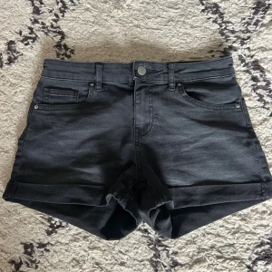 Svarta jeansshorts med uppvik - Svarta jeansshorts med klassisk femficksdesign och uppvikta benslut. Snygg modell med knapp och dragkedja framtill samt bälteshällor. Perfekta för en chill och stilren look under varma dagar.
