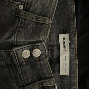 Grå bootcut jeans från Bershka - Snygga grå jeans från Bershka med bootcut-modell och låg midja. Jeansen har klassisk femficksdesign, silverfärgade knappar och är tillverkade i stretchigt denim för en bekväm passform. Perfekta för dig som gillar en stilren och trendig look.