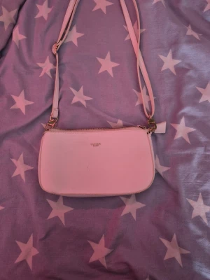 Vit axelväska från Ulrika - Säljer en stilren vit axelväska från Ulrika med justerbar rem och guldfärgade detaljer. Väskan har dragkedja upptill och flera fack inuti för kort och småsaker. Perfekt storlek för det viktigaste och enkel att matcha till olika outfits.