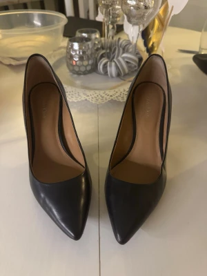 Svarta pumps från Calvin Klein - Säljer ett par klassiska svarta pumps från Calvin Klein. Skorna har spetsig tå, smal hög klack och är tillverkade i slätt skinn. Insidan är beige och de har en elegant, tidlös look som passar till allt.