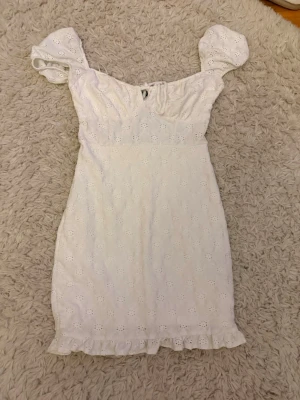 Vit kort klänning med puffärm - Söt vit kortklänning med puffärmar och broderade blommor. Klänningen har volangkant nertill och är tillverkad i ett lätt bomullstyg. Perfekt för sommarens alla tillfällen och ger en romantisk vibe. Säljer för att den har blivit för kort.