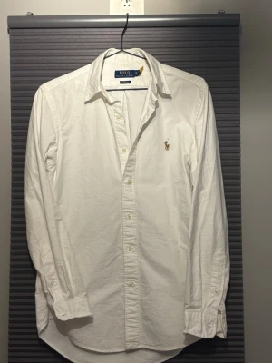 Vit skjorta från Polo Ralph Lauren XS - Klassisk vit skjorta från Polo Ralph Lauren i bomull med broderad logga på bröstet. Skjortan har lång ärm, knappar framtill och klassisk krage. Classic fit-modell som passar till allt och ger en clean look. Väldigt sparsamt använd och nypris ligger på runt 1600kr. Priset är inte hugget i sten!!
