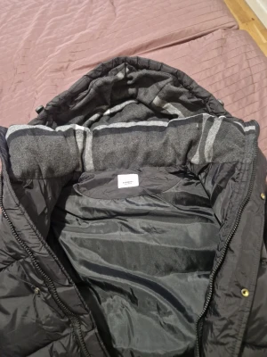 Svart pufferjacka från Burberry - Säljer en svart pufferjacka från Burberry med avtagbara ärmar så den kan bäras som väst. Jackan har huva, stora fickor med dragkedja och Burberry London England-logga på ärmen. Perfekt för kalla dagar och riktigt snygg streetstil.