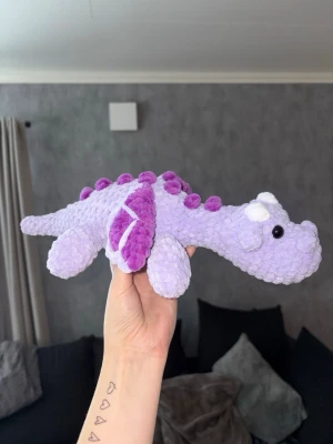 Virkad lila drake 🐉💜  - Virkad lila drake – handgjord & unik 🐉💜 En charmig och mjuk virkad drake i lila toner, perfekt som present, inredningsdetalj eller gosedjur för större barn • Draken är stadig men samtidigt mjuk och kramvänlig, och passar lika bra i barnrummet som på hyllan eller sängen✨ 🐉Pris: 350kr 🐉OBS! ⚠️ Innehåller säkerhetsögon – rekommenderas ej till barn under 3 år.