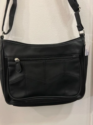 Oanvänd svart axelväska från Nicole - Oanvänd snygg svart axelväska från Nicole i skinnimitation med flera praktiska fack och dragkedjor. Väskan har justerbar axelrem och stilrena sömdetaljer på framsidan. Perfekt för dig som vill ha ordning på dina grejer och ändå se cool ut.😍❤️🥰