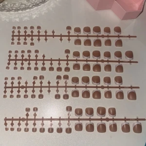 Bruna tå-lösnaglar i olika storlekar - Säljer ett set med tånagla lösnaglar i flera storlekar. Naglarna har en matt finish och en naturlig fyrkantig form. Perfekta för att fixa snygga naglar snabbt hemma. Kommer på plastställ för enkel applicering.