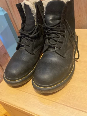 Svarta Dr. Martens boots med foder - Säljer ett par svarta Dr. Martens boots i skinn med varmt grått foder. Klassisk gul söm runt sulan, grov sula och snörning framtill. Perfekta för kalla dagar och ger en cool vibe till vilken outfit som helst. Flitigt använda men mycket kvar att ge, hälkapporna slitna men enkelt att fixa😊