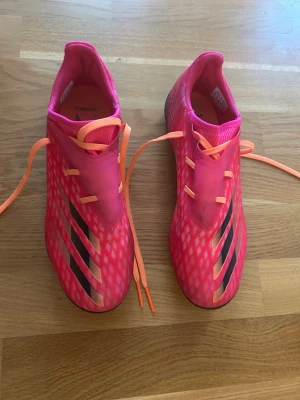 Adidas rosa fotbollsskor strl 39⅓ - Säljer ett par grymt snygga Adidas fotbollsskor i stark rosa med orange snören och svarta detaljer. Skorna har ett mönstrat mesh-överdrag och klassiska tre ränder på sidan. Lätta och smidiga med dobbar för bra grepp på planen. Använda 3-5 ggr. För övrigt mycket bra skick