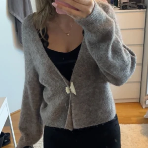 Beige stickad kofta från Lindex - Mysig beige stickad kofta från Lindex i storlek XS. Koftan har en croppad design och långa ärmar, perfekt för kyliga dagar. Den är tillverkad i ett mjukt material som ger en skön känsla. Ett stilrent plagg som passar till många olika outfits.