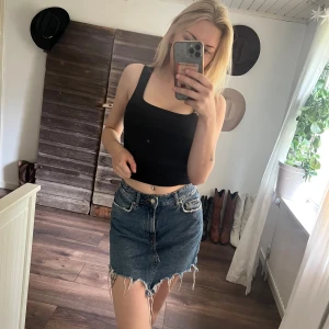  jeanskjol - Säljer en blå jeanskjol med rå, fransig nederkant och klassiska fickor fram och bak. Kjolen har en kort passform och stängs med knapp och dragkedja. Perfekt för dig som gillar en avslappnad och trendig stil.