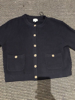 Mörkblå stickad kofta från H&M - Säljer en mörkblå stickad kofta från H&M med snygga guldknappar framtill och på fickorna. Koftan har rund halsringning, två framfickor och långa ärmar. Pris kan diskuteras vid snabb äffar! 