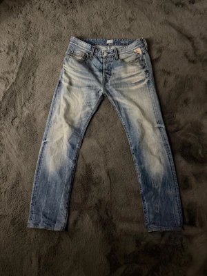 Replay jeans - Säljer ett par ljusblå Replay jeans med snyggt slitna detaljer och klassisk femficksdesign. Jeansen har raka ben och normal passform, med Replay-logga på fickan fram och patch bak i midjan. Perfekta för dig som gillar en avslappnad men ändå stilren look. W30 L32 99cm längd 